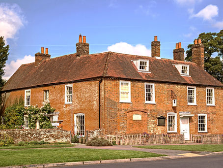 The front of Jane Austen's house which is a red brick building with flowers along the side of one wall.