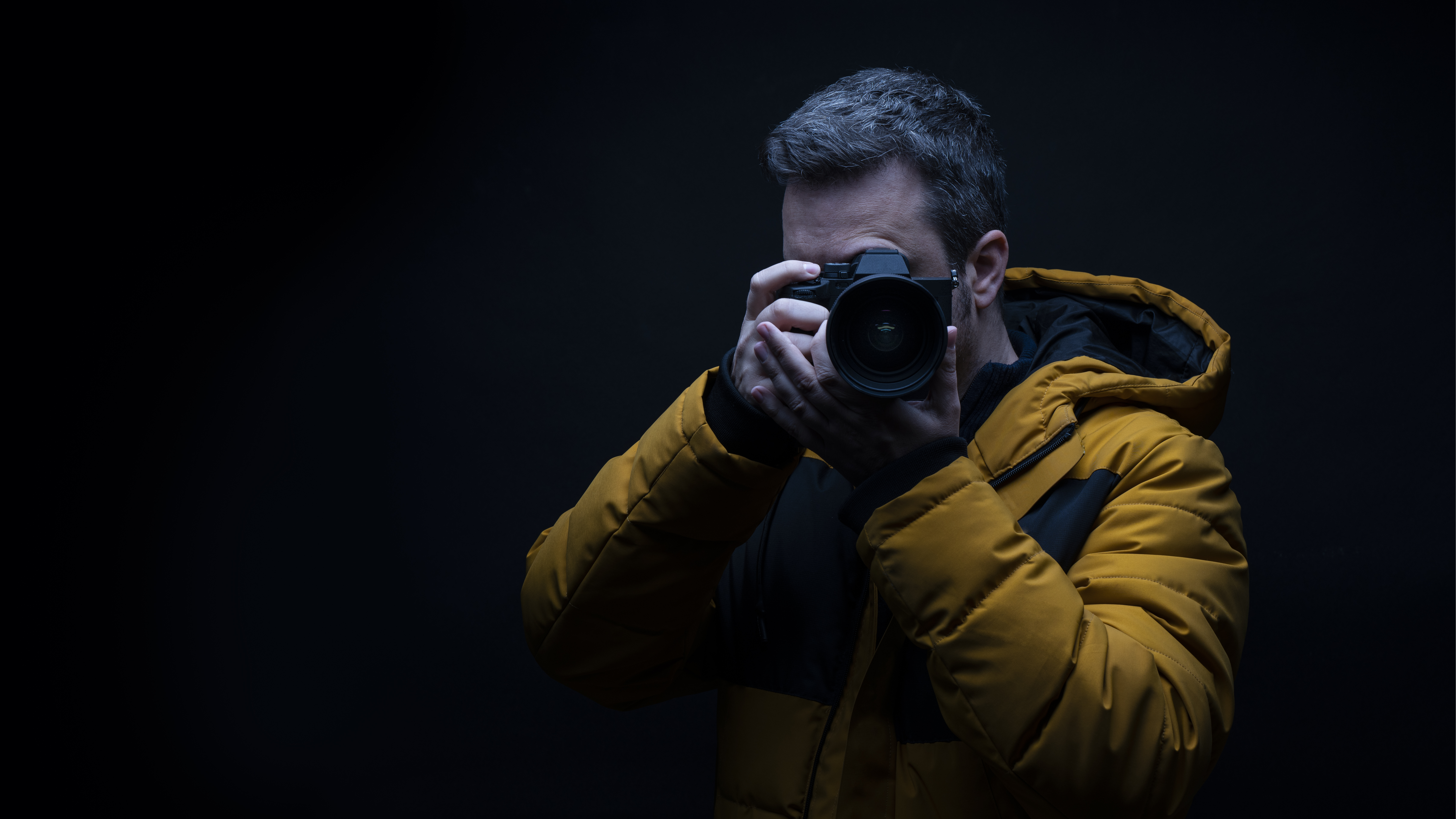 portrait-photographer-yellow-winter-coat-taking-photo-with-black-background-studio.jpg