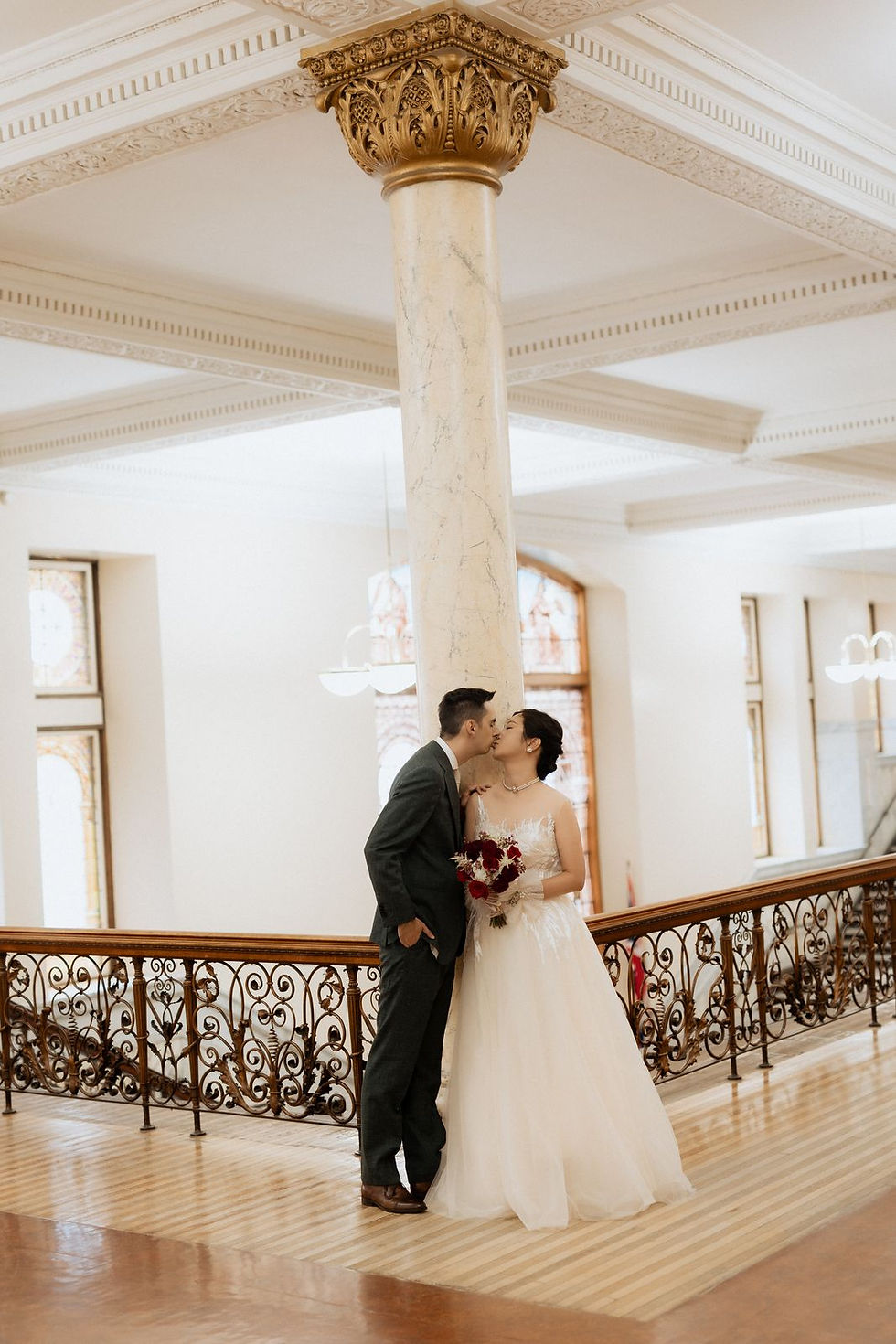 The couple kissing beside a marble column and the arched windows inside Old City Hall in Toronto.