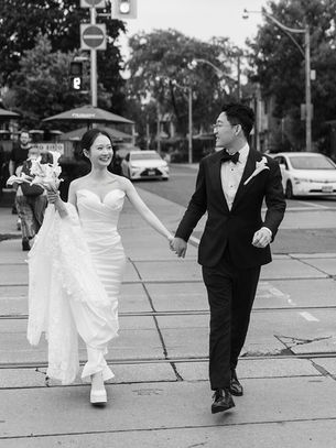 Black and white photograph of a bride and groom walking hand in hand along College Street in Toronto on their wedding day.