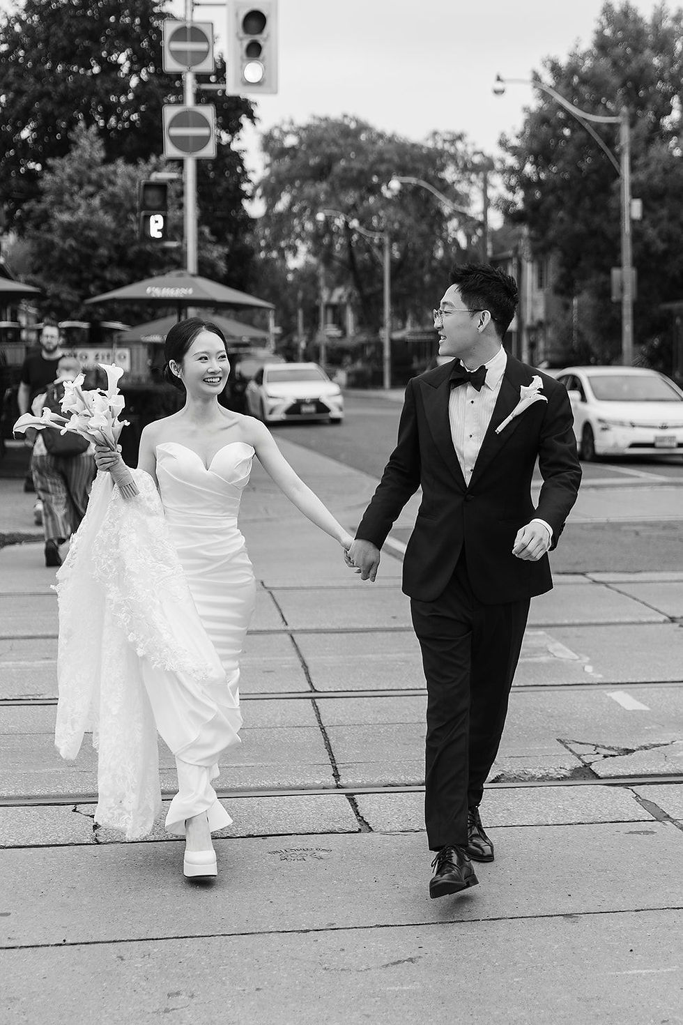 Black and white photograph of a bride and groom walking hand in hand along College Street in Toronto on their wedding day.