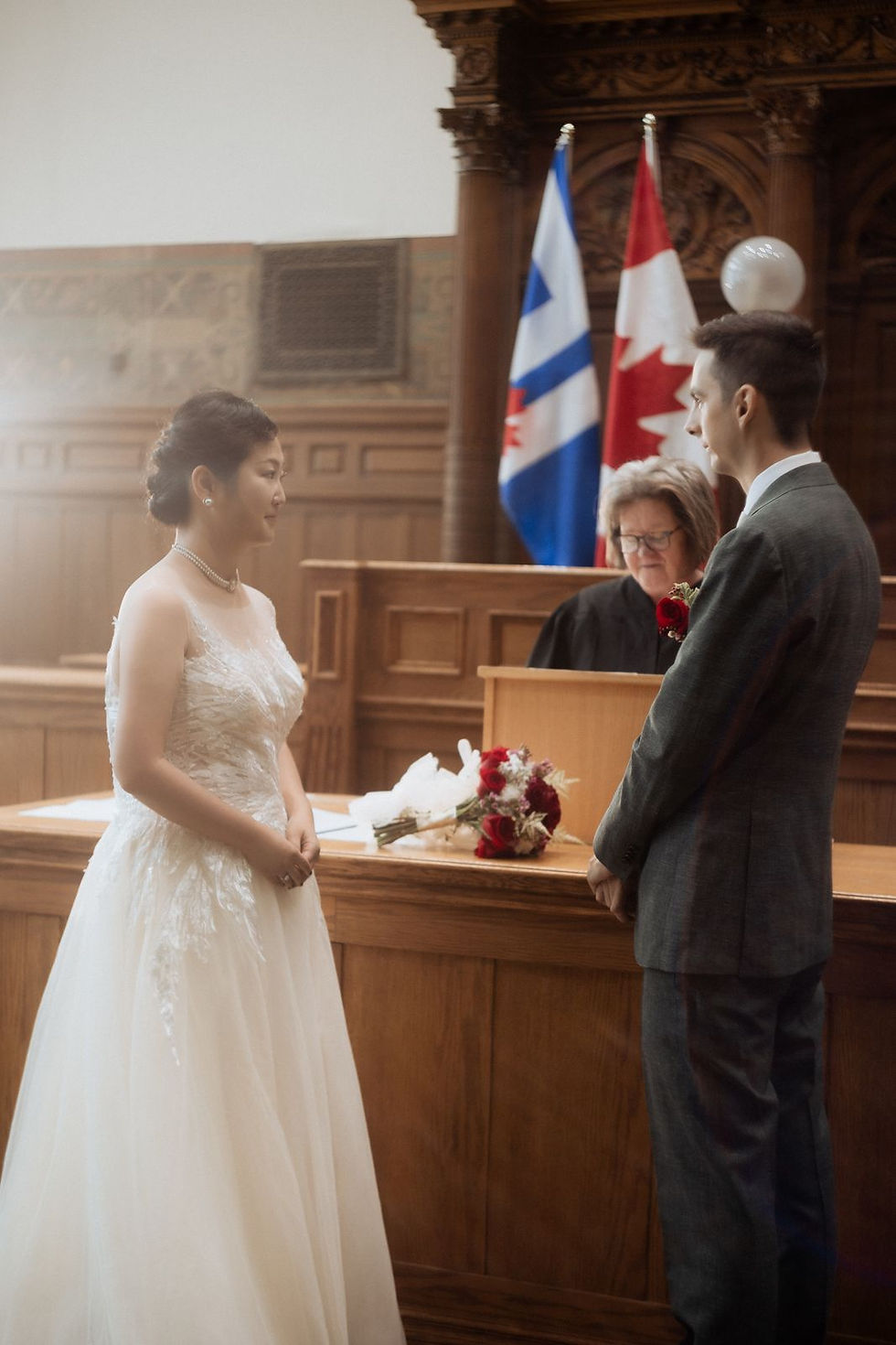 The couple at the wooden table in the Council Chamber at Old City Hall during their civil ceremony, with the officiant behind it.