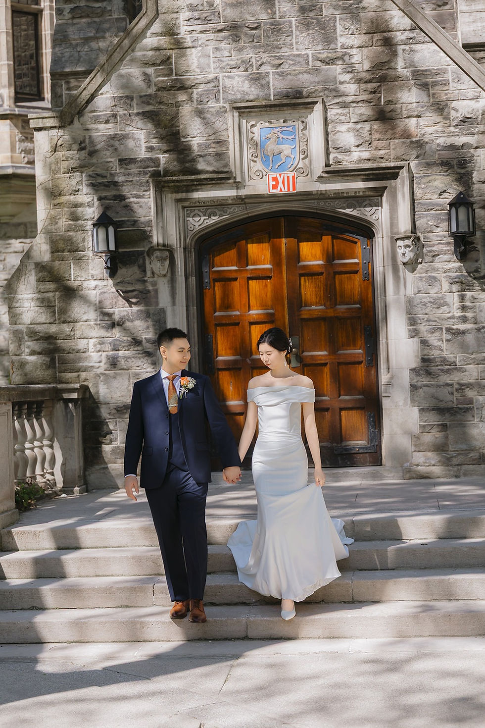 Bride and groom holding hands as they descend stone steps outside the arched wooden doors of Trinity College.