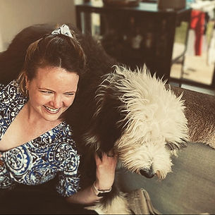 A smiling woman in a blue and white dress sitting beside a hairy black and white old english sheep dog