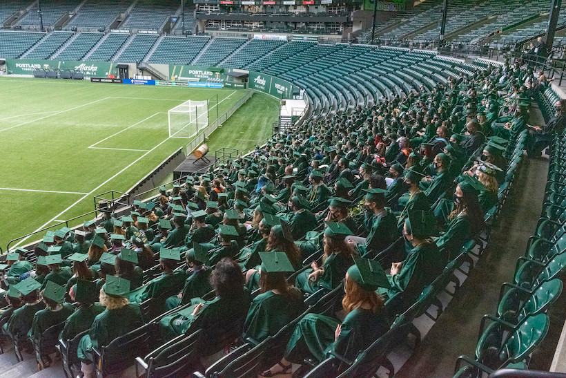 students in green graduation robes and hats seated in PGE Park