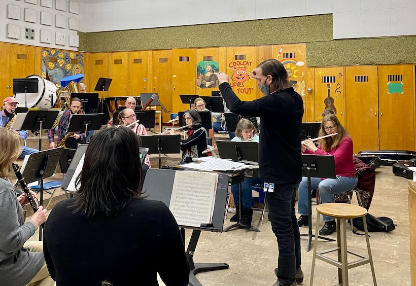 A band director wearing black in front of a symphonic band.