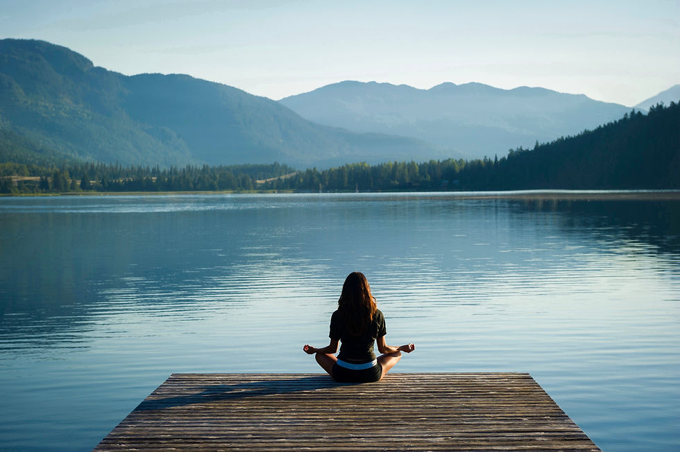 Person meditating cross‑legged on a wooden dock above a calm lake with mountains in the distance, embodying mindfulness and nature connection.