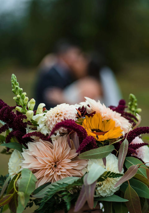 Closeup image of bridal bouquet with yelllow sunflowers, Cafe Au Lait dahlias, white snapdragons, and other fillers to incorporate deep, burgundy reds.