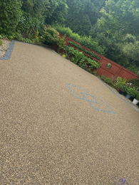 Light brown resin driveway, blue hopscotch, red fencing, green landscaping.