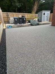 Newly installed grey resin driveway with garden shed and fencing.