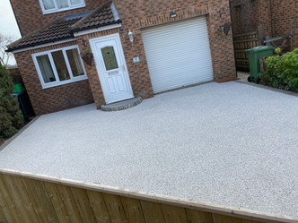 Light resin driveway path in front of modern brick house and garage.