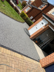 Grey resin driveway path leading to a modern brick house.