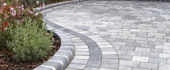 Curved block paved driveway leading to a white house entrance.