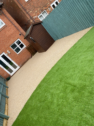 Resin path, artificial grass, brown shed, brick house, green fence landscaping.