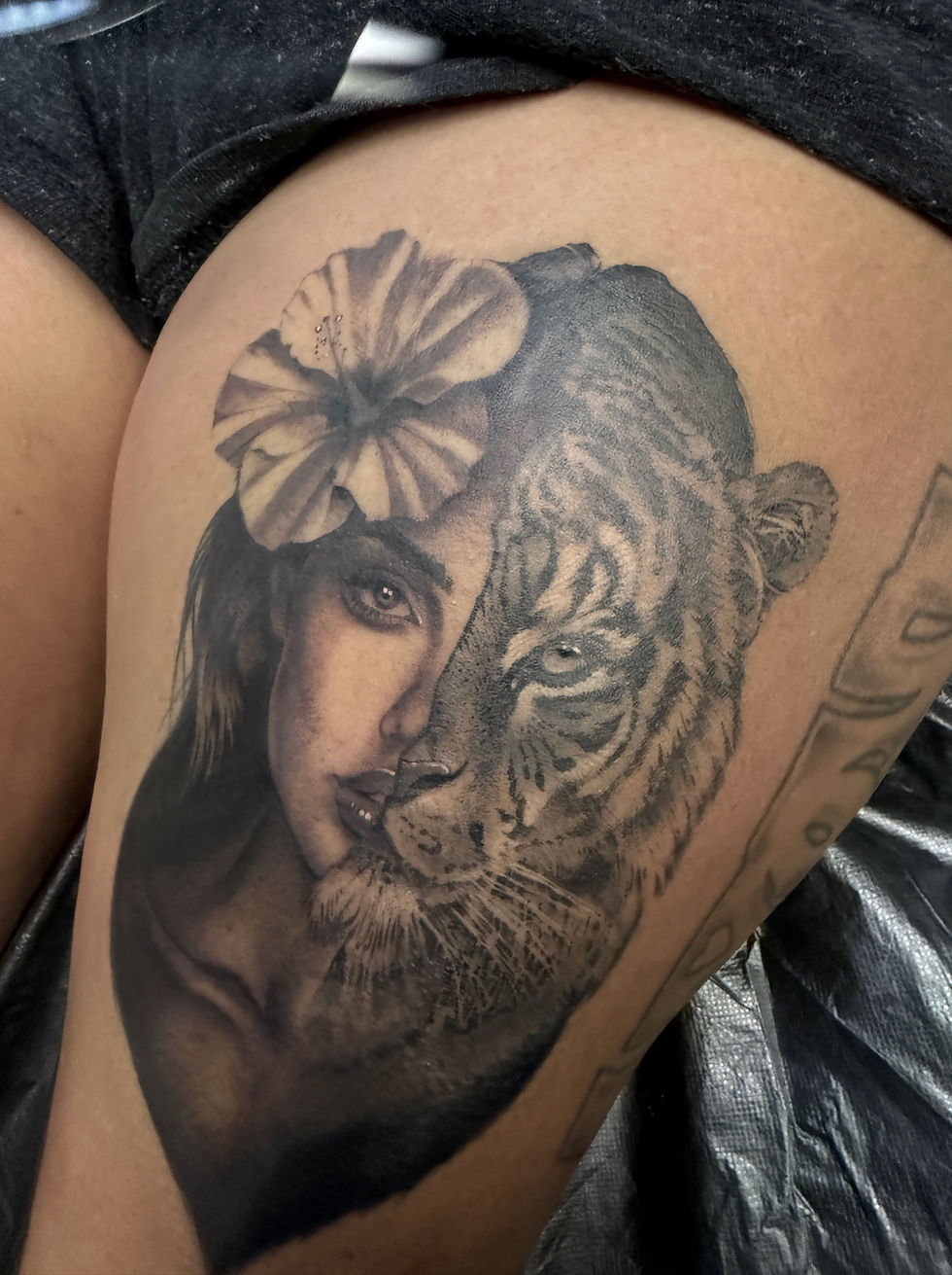 Eye-level view of a tattoo artist working on a black and grey tattoo on a client’s arm