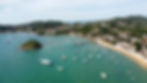 Aerial view of a picturesque coastal town, with boats dotting the turquoise waters and lush green hills surrounding the vibrant community.