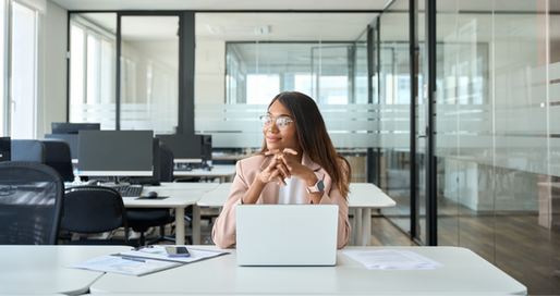 Business professional sitting at a desk in a modern office, looking thoughtful while working on a laptop, representing HR leaders planning workforce and technology strategies for 2025.