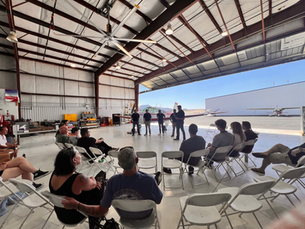 Group of attendees standing in a hangar having a discussion during the Hangar Hangout event.