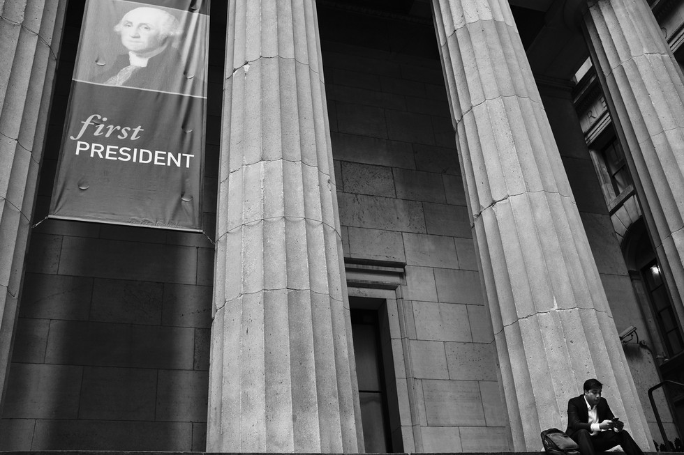 Muž sedící na schodech pod velikými sloupy před muzeem