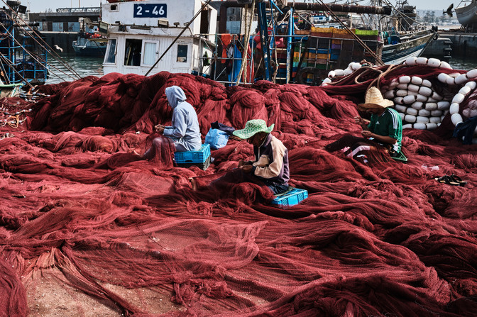 Tři muži v přístavu šijí červenou síť