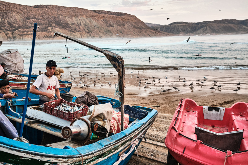 Rybář u své modré lodi s hejnem racků na pláži v pozadí