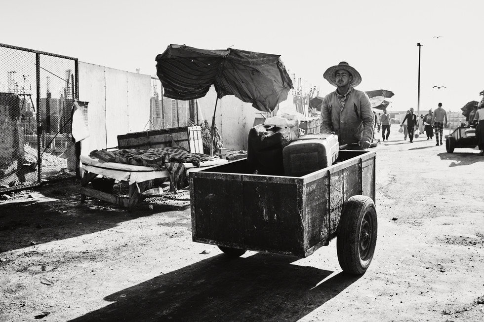 Muž v klobou tlačí vozík s krabicemi