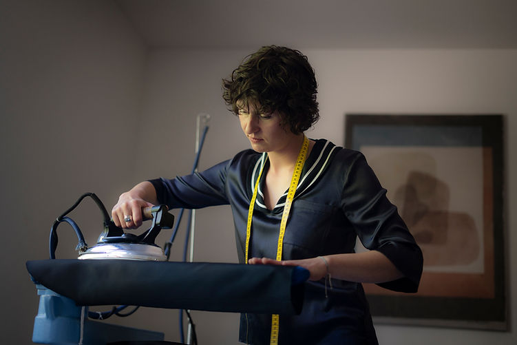 Schneiderin bügelt Stoffstück mit Bügeleisen, gelbes Maßband um den Hals hängend