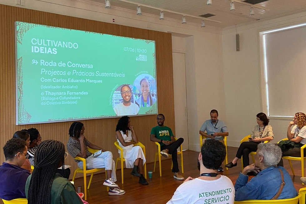 Roda de conversa Cultivando Ideias no Museu do Jardim Botânico: participantes sentados em círculo em cadeiras amarelas diante de um telão verde.