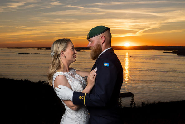 Bröllopspar med uniform som fotograferas i solnedgången under Golden Hour. Fotot är taget i göteborg nära oskar den andres fort med utsikt över göteborgs skärgård och hamn. Fotograf Oskar Gillblad.