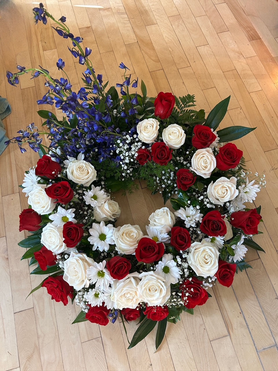Patriotic funeral urn wreath with red and white roses, white daisies, baby’s breath, and accents of deep blue delphinium, arr