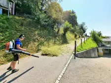 Mann mit Rucksacklaubbläser reinigt Weg von Grasschnitt am Hang