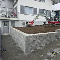 Kleiner Bagger arbeitet in einem angelegten Hochbeet vor dem Haus.