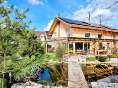 Modernes Haus mit Solaranlage, Teich und Holzbrücke im Garten.