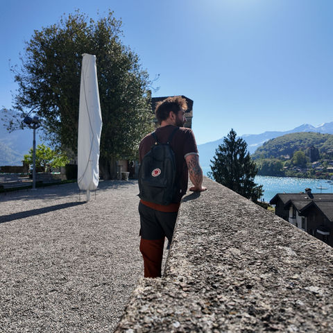 Man with backpack looking at mountain lake from stone wall.