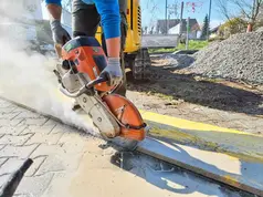 Arbeiter schneidet Pflastersteine mit Trennschleifer, Staubentwicklung auf Baustelle.