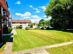 Mehrere rote Wohngebäude mit grünem Rasen und Parkplatz im Sonnenlicht.