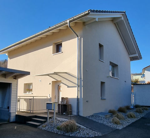 Zweigeschossiges Einfamilienhaus mit weisser Fassade, Flachdachvordach und Kiesbeet am Eingang.