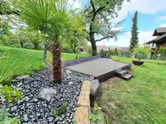 Mediterraner Garten mit Palme, gepflasterter Terrasse und schwarzem Zierkies.