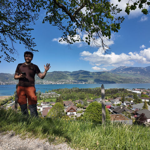 Man waving on a grassy hill overlooking a lake and town.