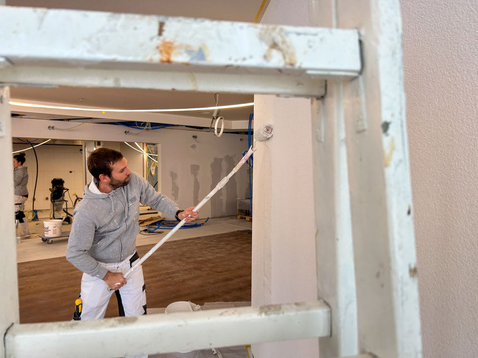 Maler streicht mit der Farbrolle durch ein Gitter hindurch eine Wand.
