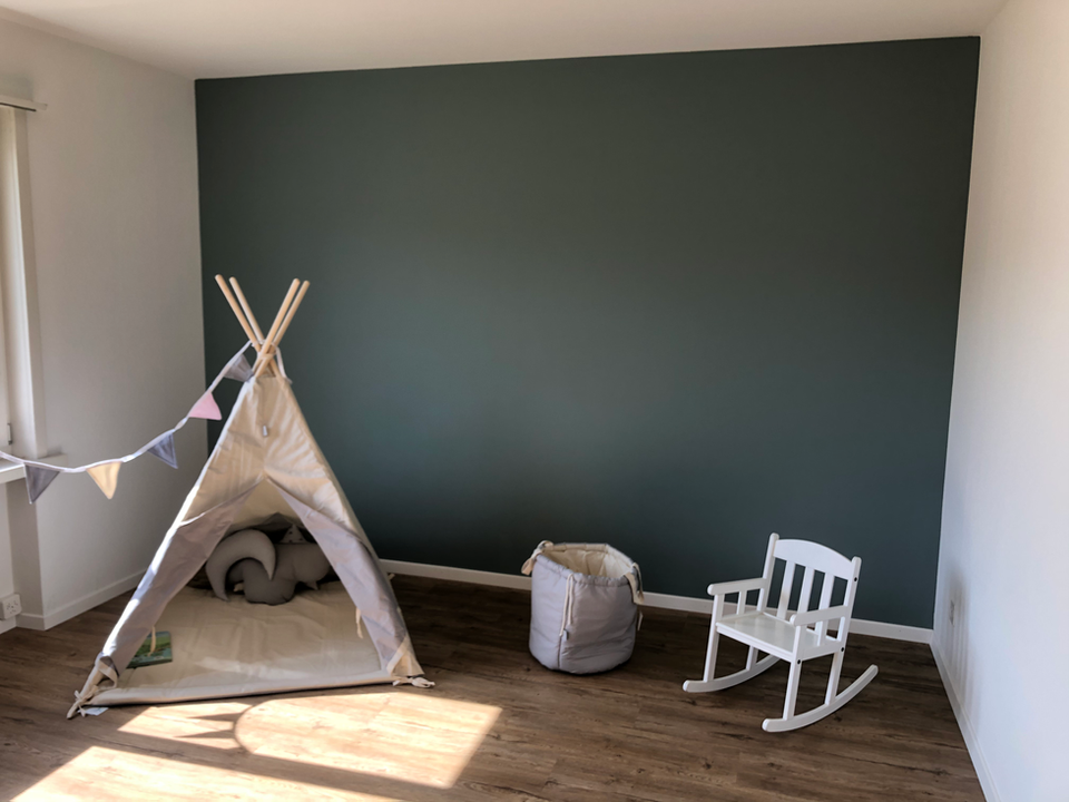 Kinderzimmer mit dunkelgruen gestrichener Wand, Tipi-Zelt und Schaukelstuhl.