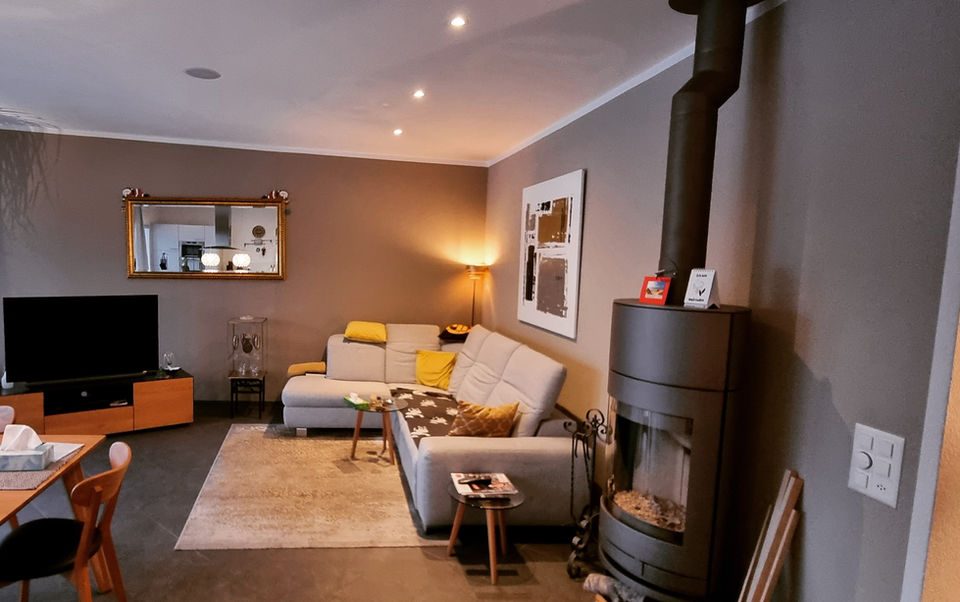 Modernes Wohnzimmer mit Kaminofen, Sofa, Fernseher und warmem Licht.
