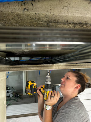 Handwerkerin befestigt eine Deckenlampe in einem Technikraum.