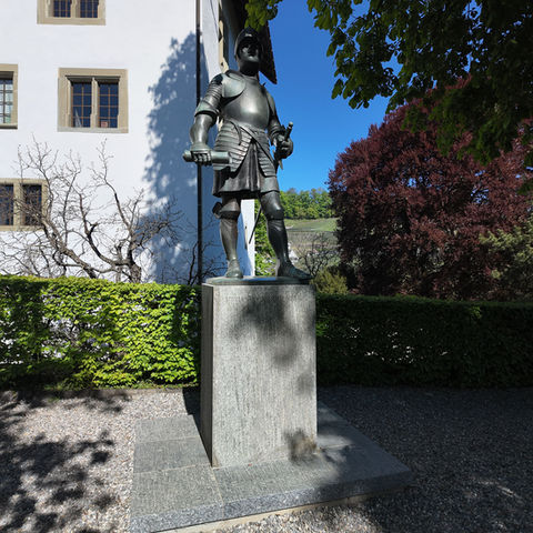Bronze knight statue in armor on a stone pedestal outdoors