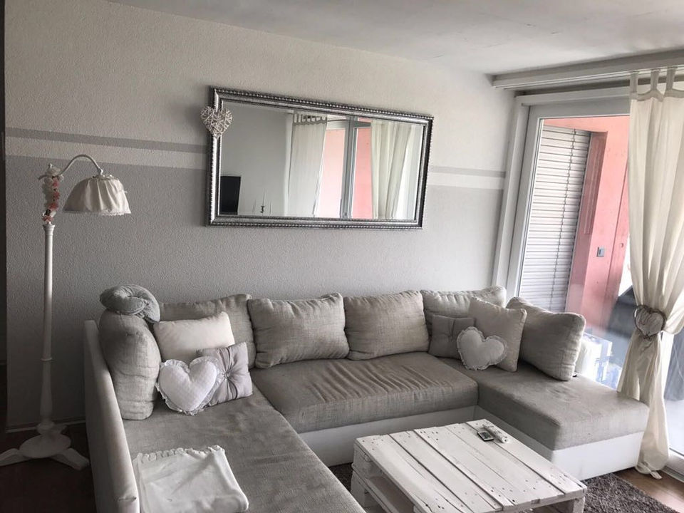 Wohnzimmer mit grossem grauen Sofa, Wandspiegel und heller Einrichtung.
