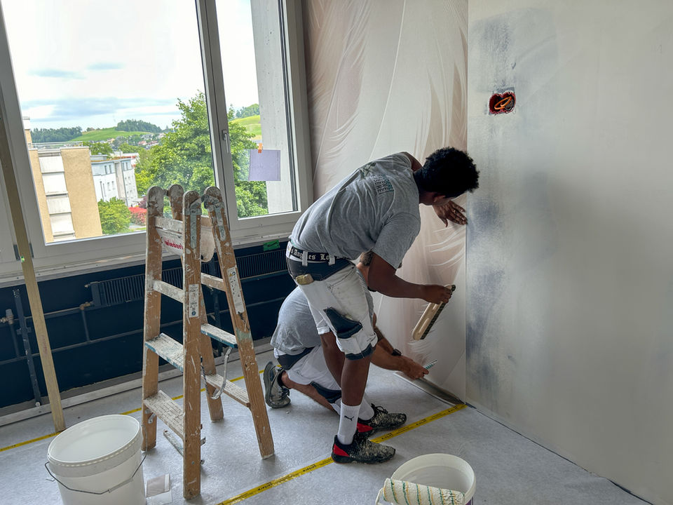 Maler auf Leiter tapeziert eine Wand in einem hellen Raum.