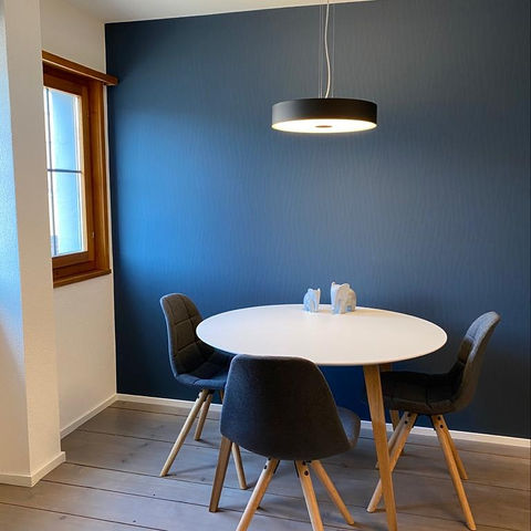 Moderner Raum mit blauer Akzentwand und rundem Tisch mit vier Stuehlen.