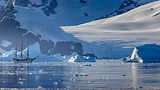Tall ship sailing past icebergs in cold, blue Antarctic water.