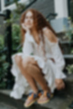 fashion photoshoot in Amsterdam A red haired curly woman in white dress sitting on stairs