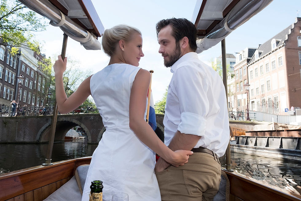 Couple in white clothing embracing on a canal boat, with Amsterdam-style buildings and bridge in the background - photographed by Amsterdam photographer
